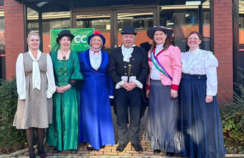 Group in historical costumes outside red brick building.