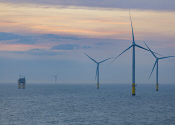 Offshore wind turbines at sunset over ocean.