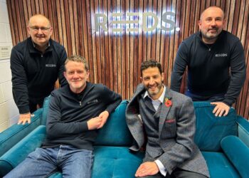 Four smiling men in branded clothing, seated indoors.