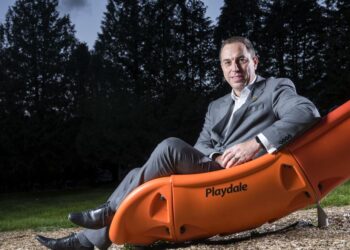 Man in suit sitting on orange playground slide.