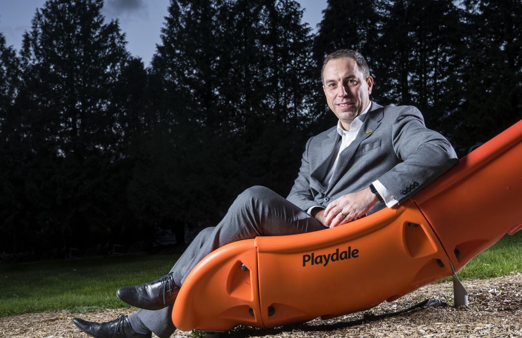Man in suit sitting on orange playground slide.