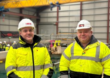 Two construction workers in high-visibility jackets indoors.