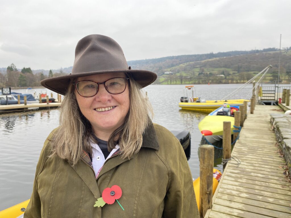 Smiling person by a lake with boats in background.