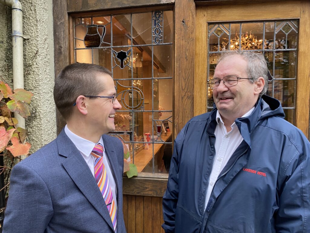 Two men smiling outside a stained glass door.