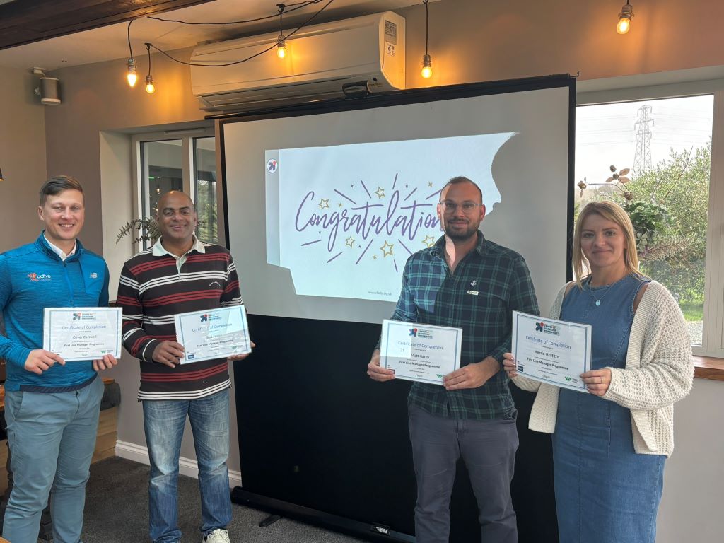 Four people holding certificates at congratulations event.