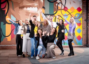 Group posing energetically in front of colourful mural.