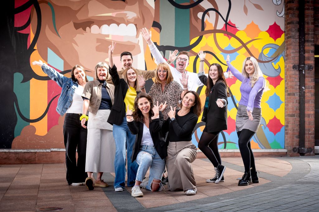 Group posing energetically in front of colourful mural.