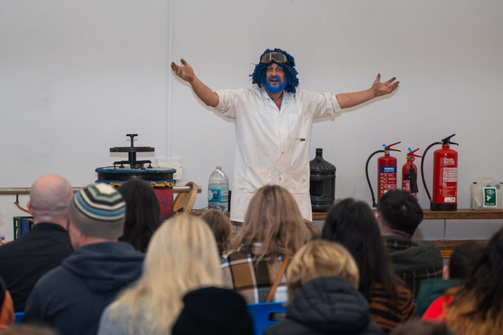 Performer in white coat entertaining audience with props.