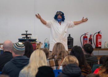 Performer in white coat entertaining audience with props.