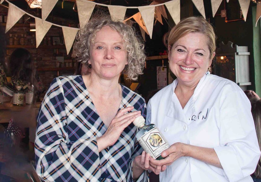 Two women smiling, holding a bottle in pub.